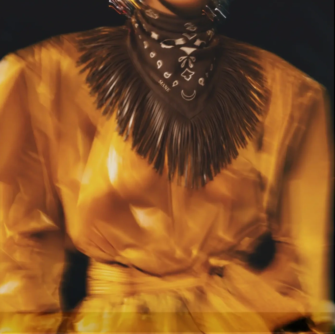 Model in a golden trench coat wearing the Marlow scarf in Bark with its faux leather fringe